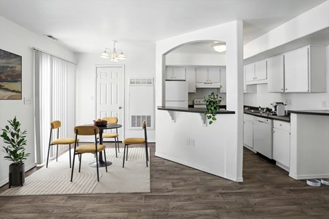 A dining area with a table and chairs is in the foreground of a kitchen.