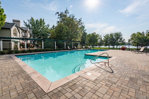A swimming pool surrounded by a brick patio and a fence at Edgewater Apartments Boise, Boise