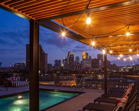 A rooftop pool area with a view of the city skyline at dusk.