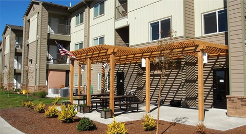 an outdoor patio with a wooden pergola in front of an apartment building