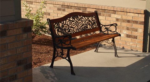 a wood and wrought iron park bench sitting in front of a brick wall