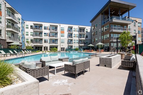 A pool area with lounge chairs and umbrellas in front of apartment buildings.