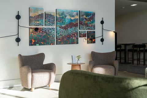 A living room with a green couch, two chairs, and a large painting on the wall.