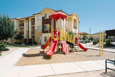 A playground with a red slide in front of a building.