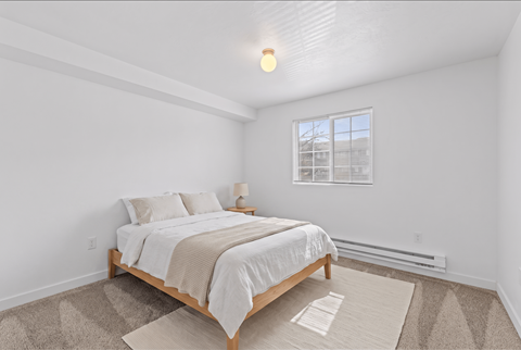A bedroom with a bed, nightstand, and window.