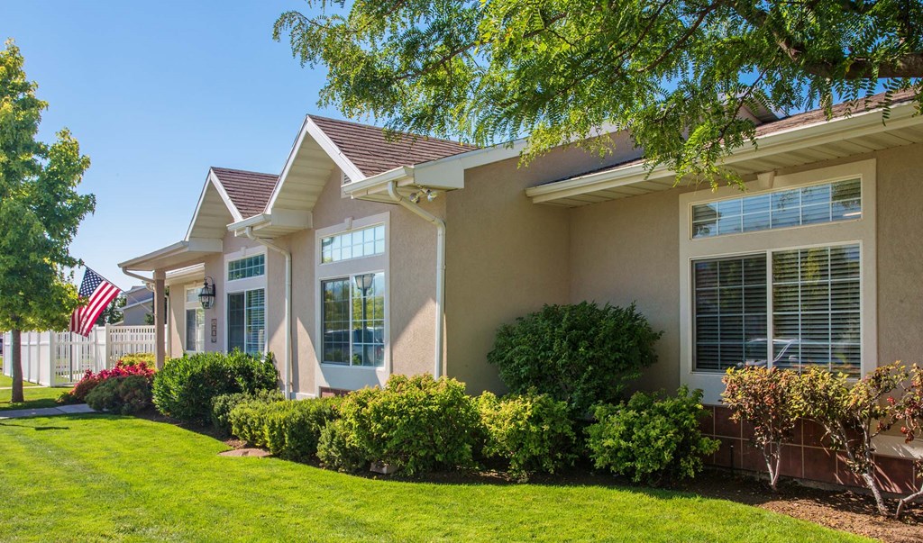 Side view of Oakstone Apartments leasing office with manicured green lawn and shrubbery lining the walls, while large, oversized windows look out into the grass at Oakstone Apartments in Clearview, UT