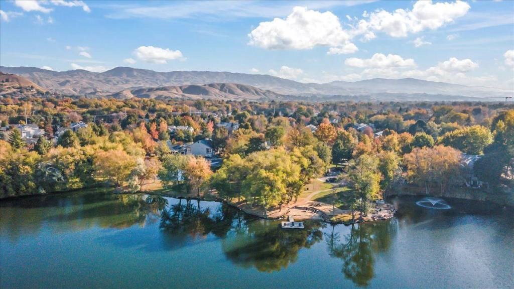 A serene landscape with a lake, trees, and a small house.