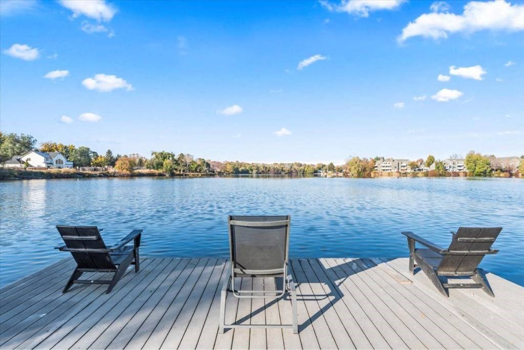 Three chairs are placed on a wooden deck by the water.