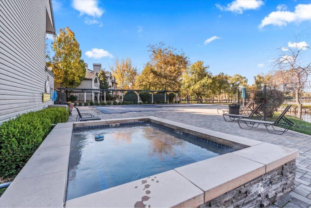 A small pool with a stone border is surrounded by a concrete patio.