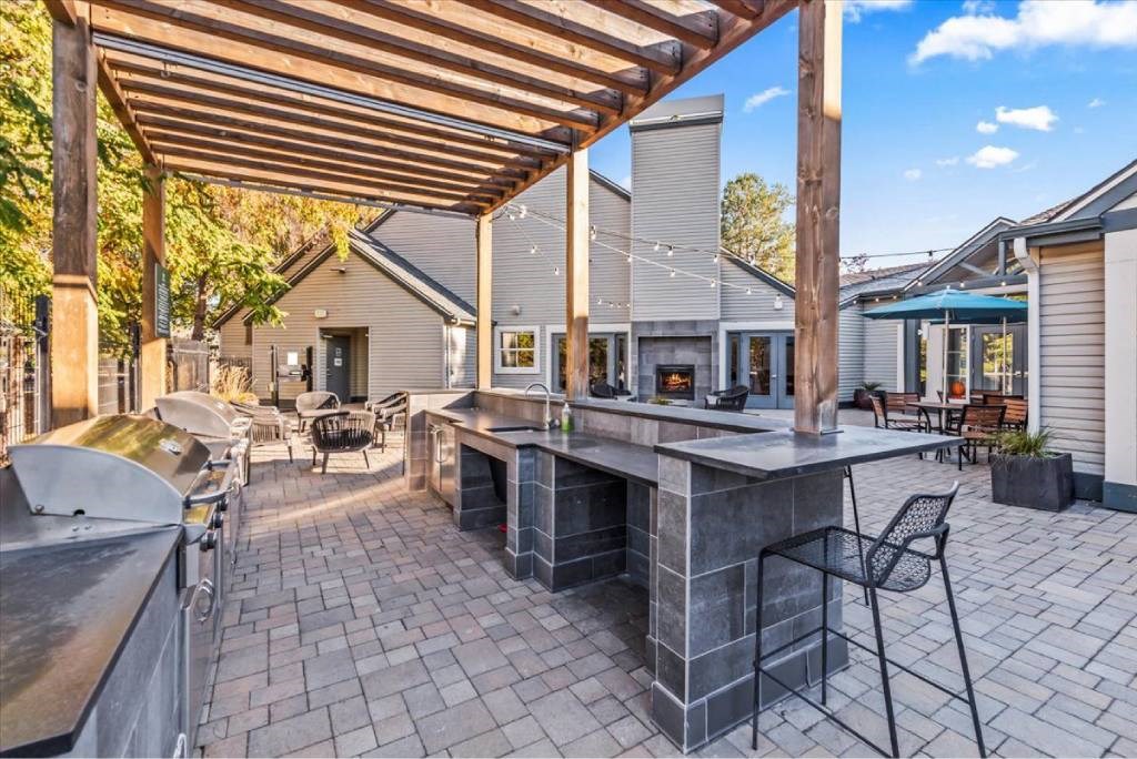 A patio with a barbecue grill and a table under a wooden pergola.