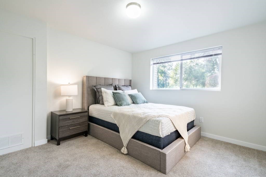 A bedroom with a bed, nightstand, and window.