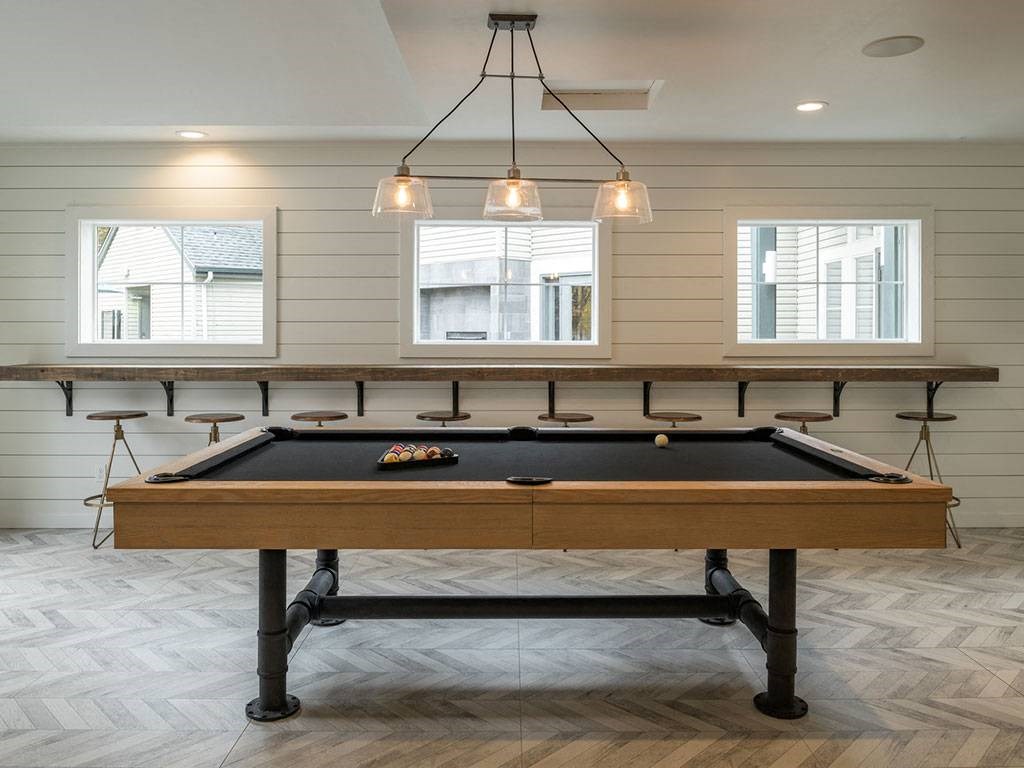 A pool table in a room with light wood flooring and two windows.