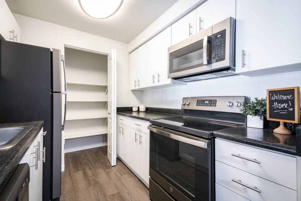 A kitchen with black and white appliances and a wooden floor.