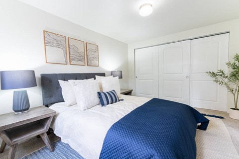 A bedroom with a bed covered in a blue comforter and a white wall.