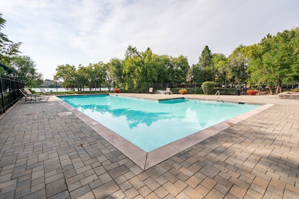 A large outdoor swimming pool surrounded by a brick patio and trees.