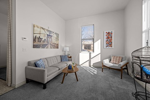 A living room with a grey couch and a painting on the wall.