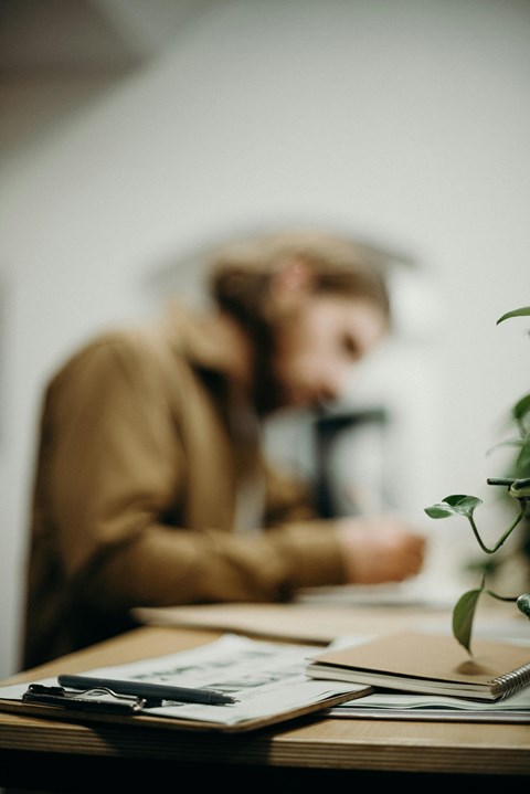 A person is sitting at a desk with a notebook and a pen in front of them.