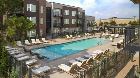 a swimming pool with lounge chairs in front of an apartment building at Cycle Apartments, Fort Collins, CO