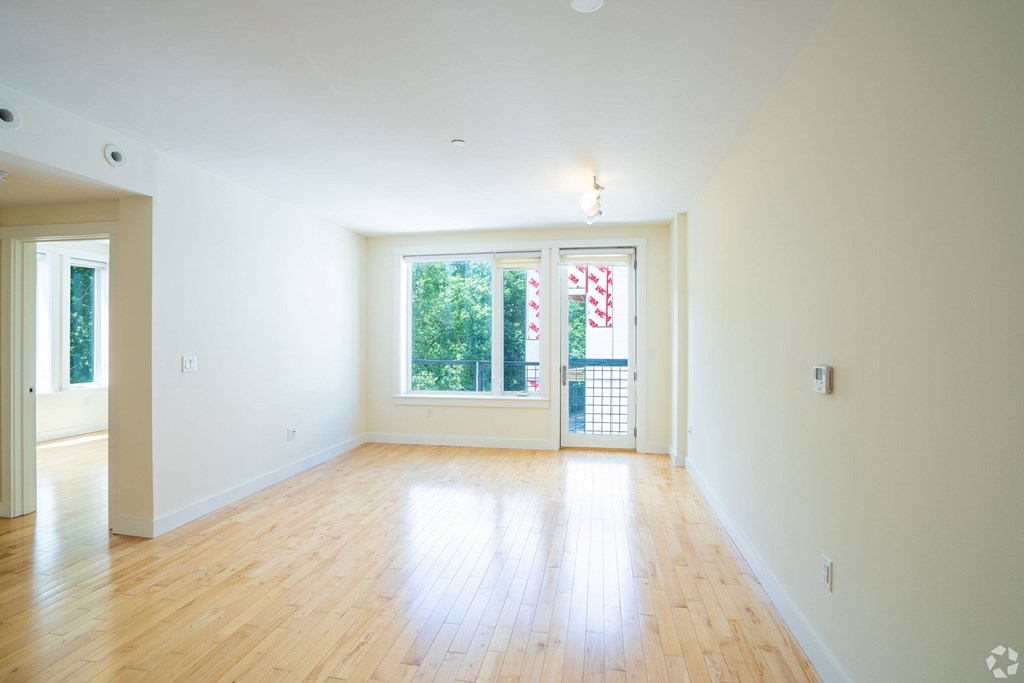 A room with wooden floors and a large window with a view of trees and a building outside at 603 Concord Apartments, Massachusetts, 02138