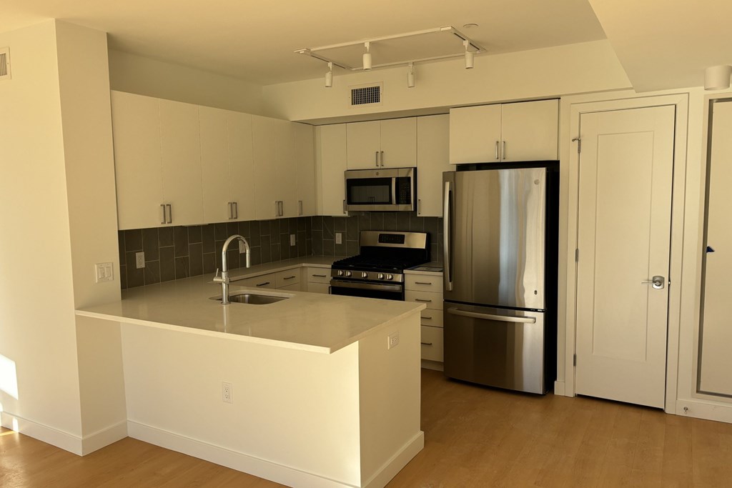 A kitchen with a stainless steel refrigerator and a microwave above the stove at 605 Concord at Fresh Pond Apartments, Cambridge, Massachusetts