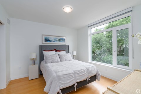 A bedroom with a large bed and a window overlooking trees  at 605 Concord at Fresh Pond Apartments, Massachusetts