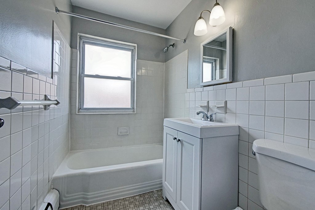 a bathroom with white tiled walls and floors and a white bathtub with a shower curtain