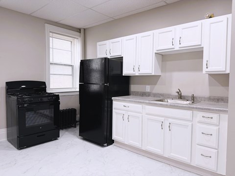 A black refrigerator stands in a kitchen with white cabinets.