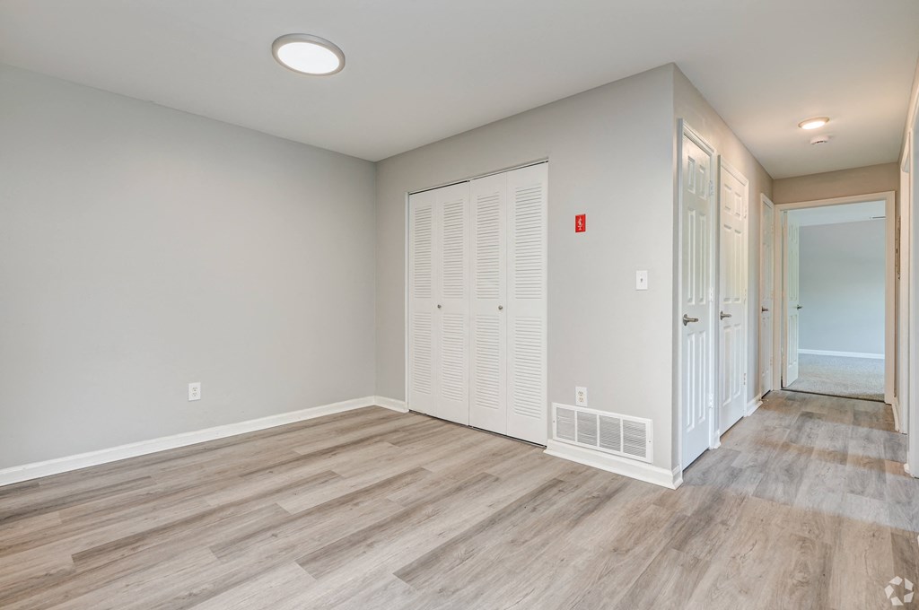 an empty room with a door to a closet and a hallway with wood flooring