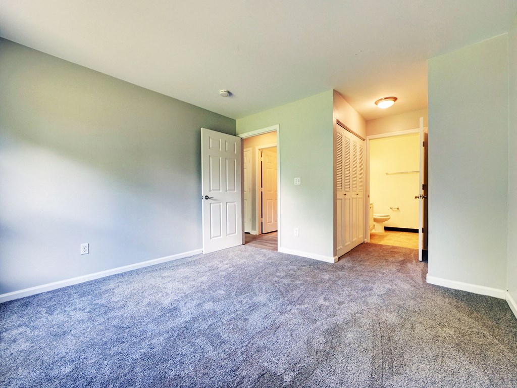 an empty living room with carpet and a door to a bathroom