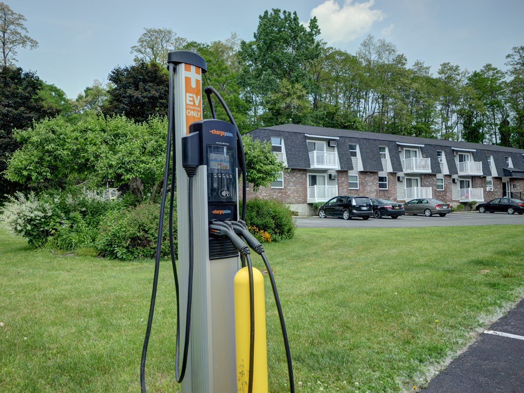 An electric vehicle charging station is located in a grassy area near apartment buildings.
