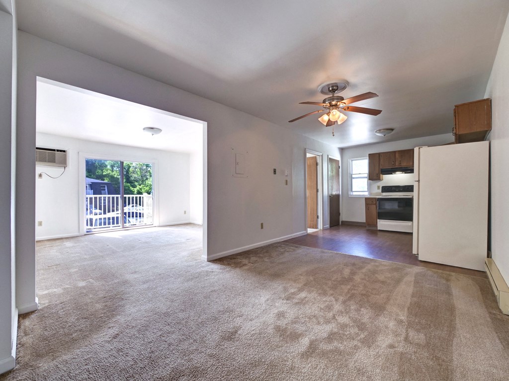 an empty living room with a ceiling fan and a kitchen