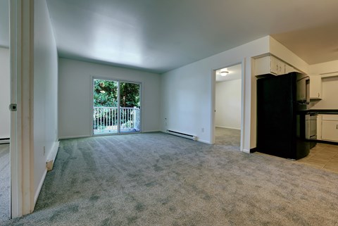 A spacious living room with a carpeted floor and a view of a fence and trees through a window.