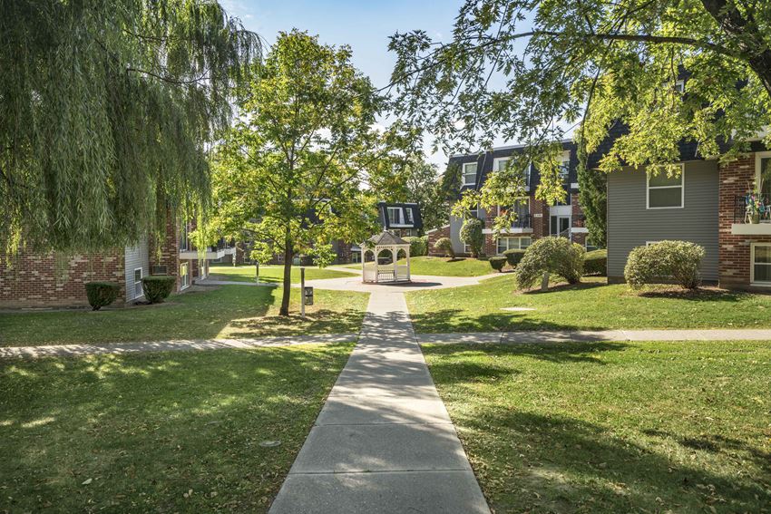 a sidewalk in front of houses with trees and a fountain