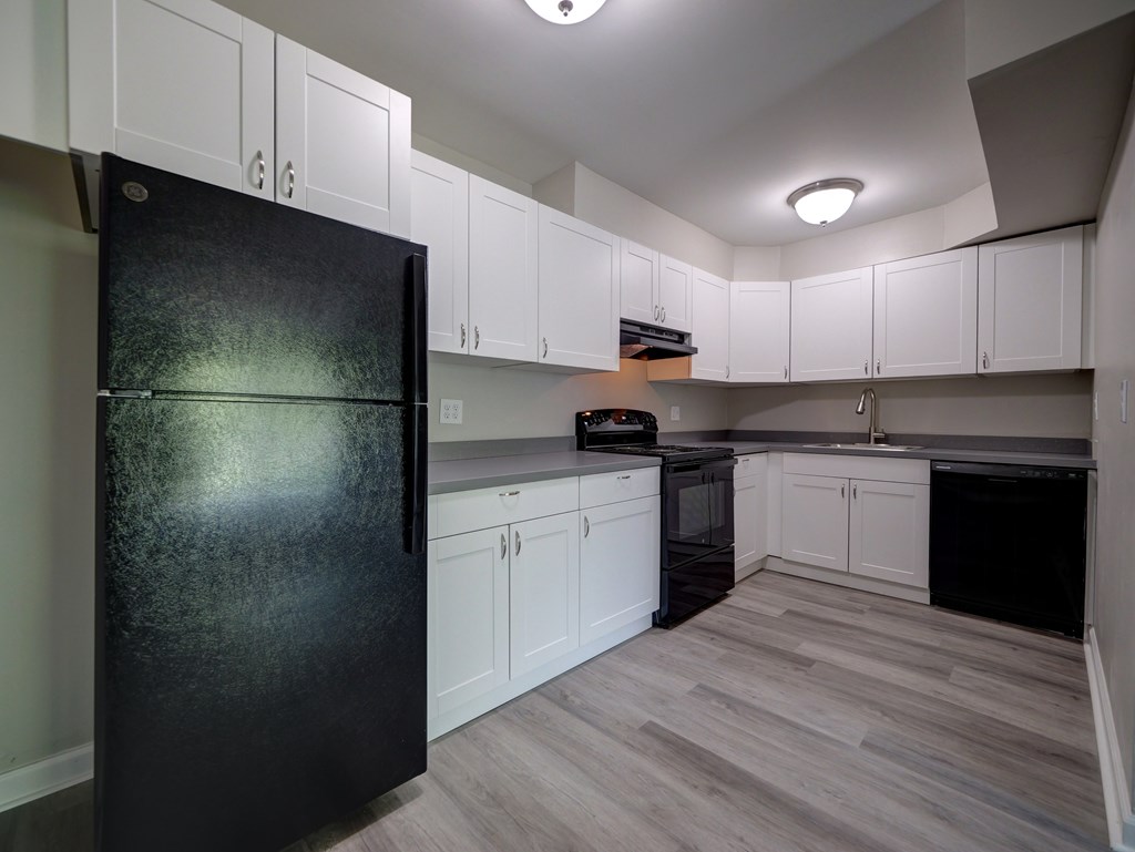 A black fridge in a kitchen with white cabinets.