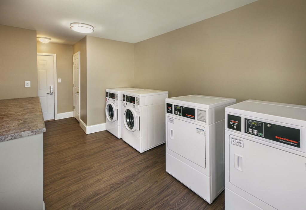 a laundry room with four washes and dryers on a wood floor