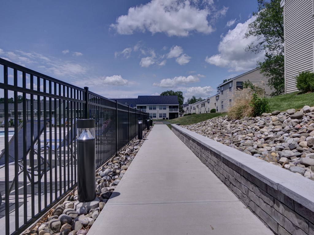 a sidewalk with a black fence and rocks next to a river