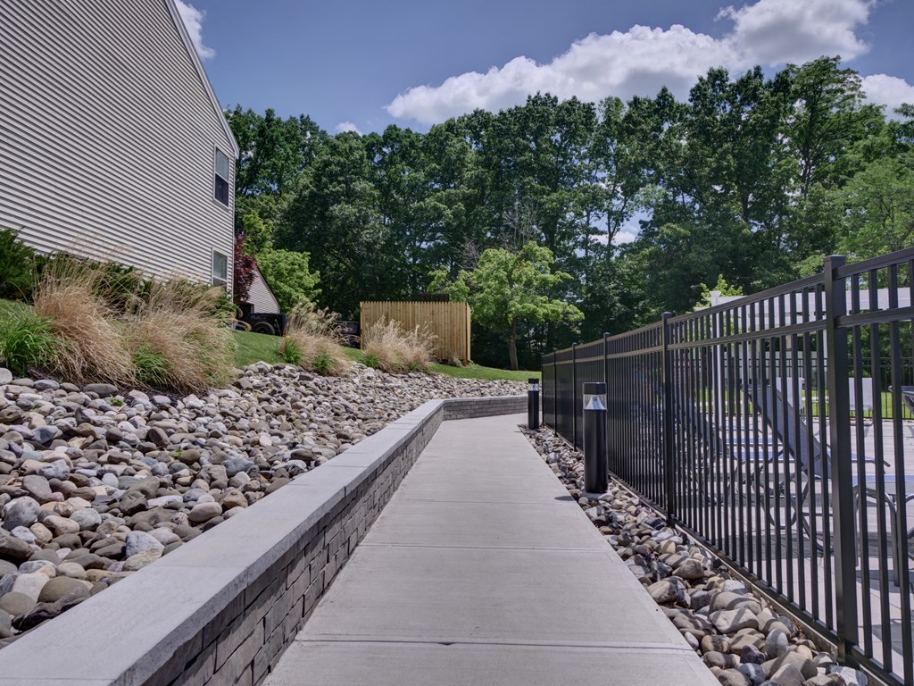 a walkway with a black fence and rocks and grass