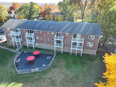 A red and white building with a black roof and a courtyard with red tables.