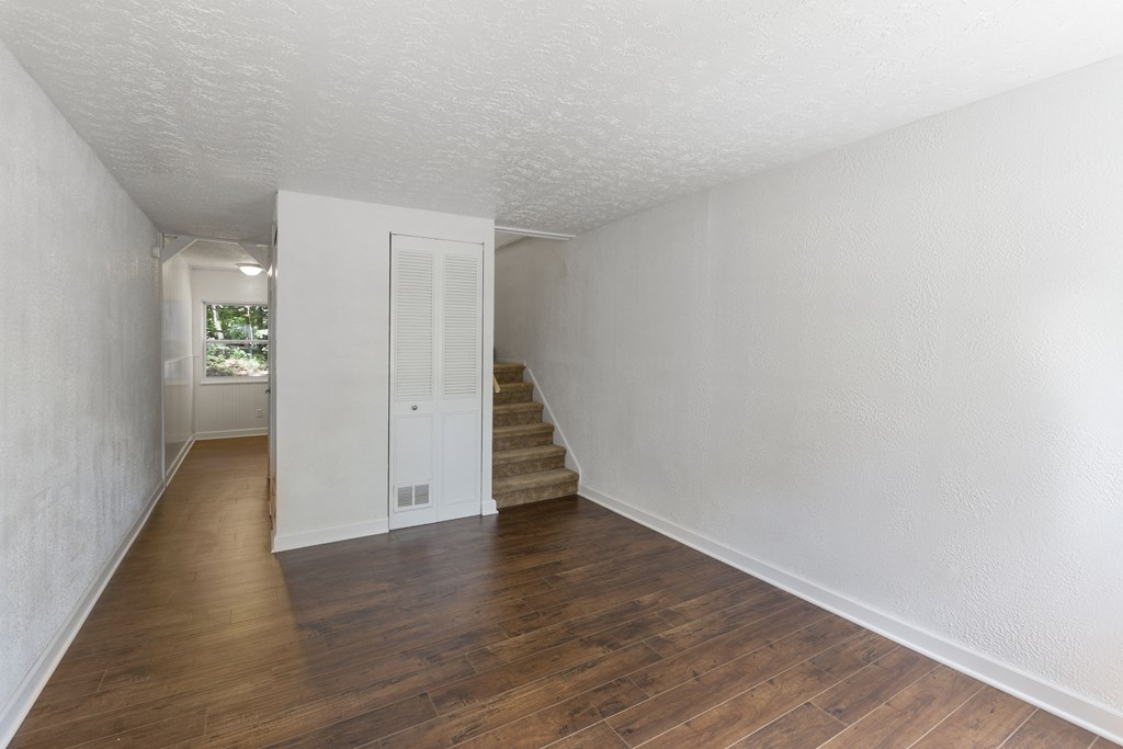an empty living room and hallway with hardwood flooring and white walls