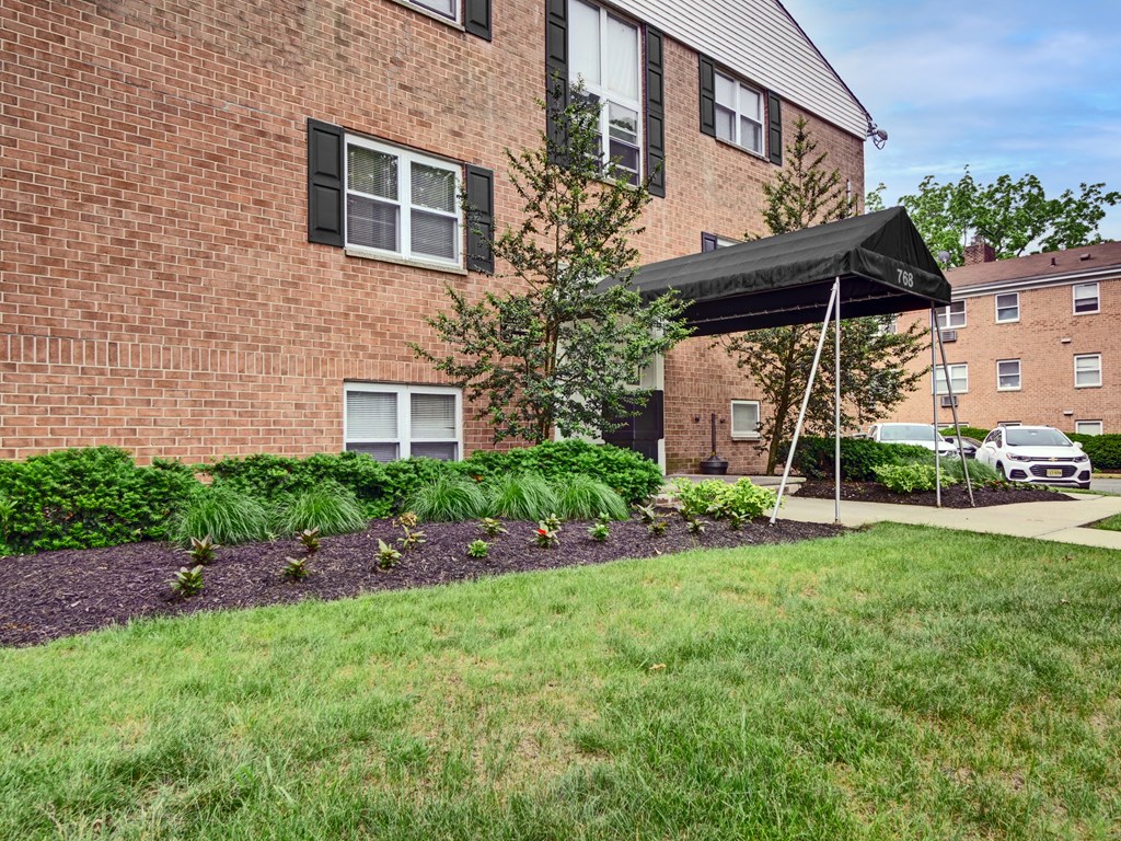 A brick building with a black awning and a tree in front.