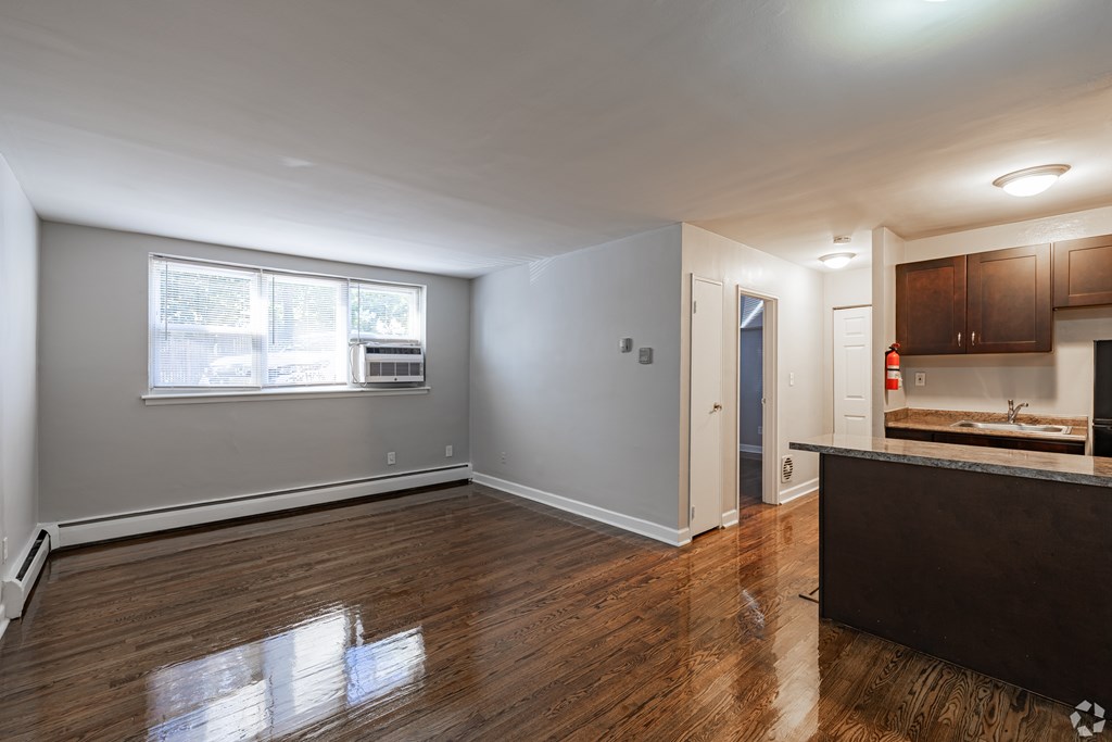 A spacious room with wooden floors and a kitchen area with a sink and cabinets.