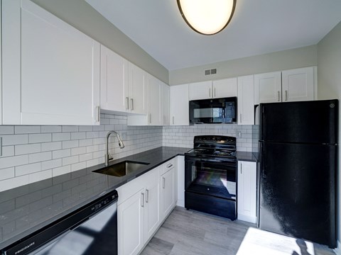 A black refrigerator sits in a kitchen with white cabinets and a black dishwasher.