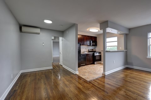 A room with wooden floors and a kitchen area in the background.