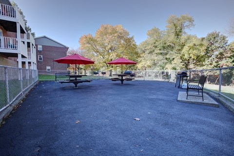 A park area with a bench and a table with a red umbrella.