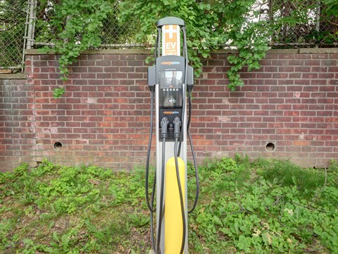 A yellow and black electric vehicle charging station sits in front of a brick wall.