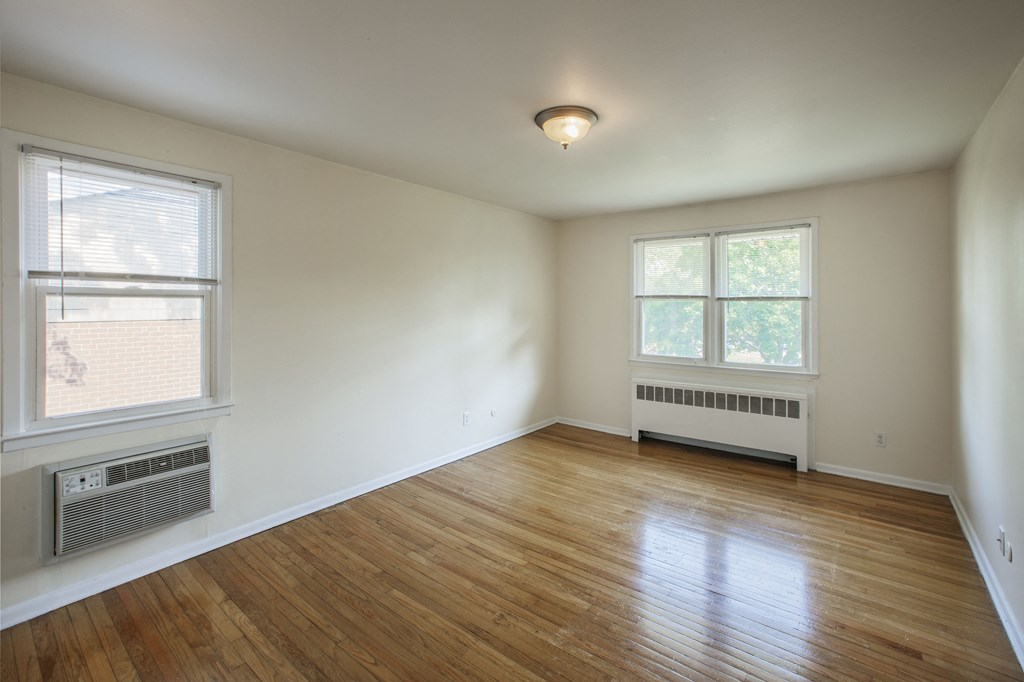 the living room of an empty house with wood floors and a radiator and two windows