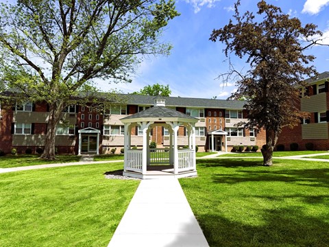 A small white gazebo is in the middle of a grassy area in front of apartment buildings.