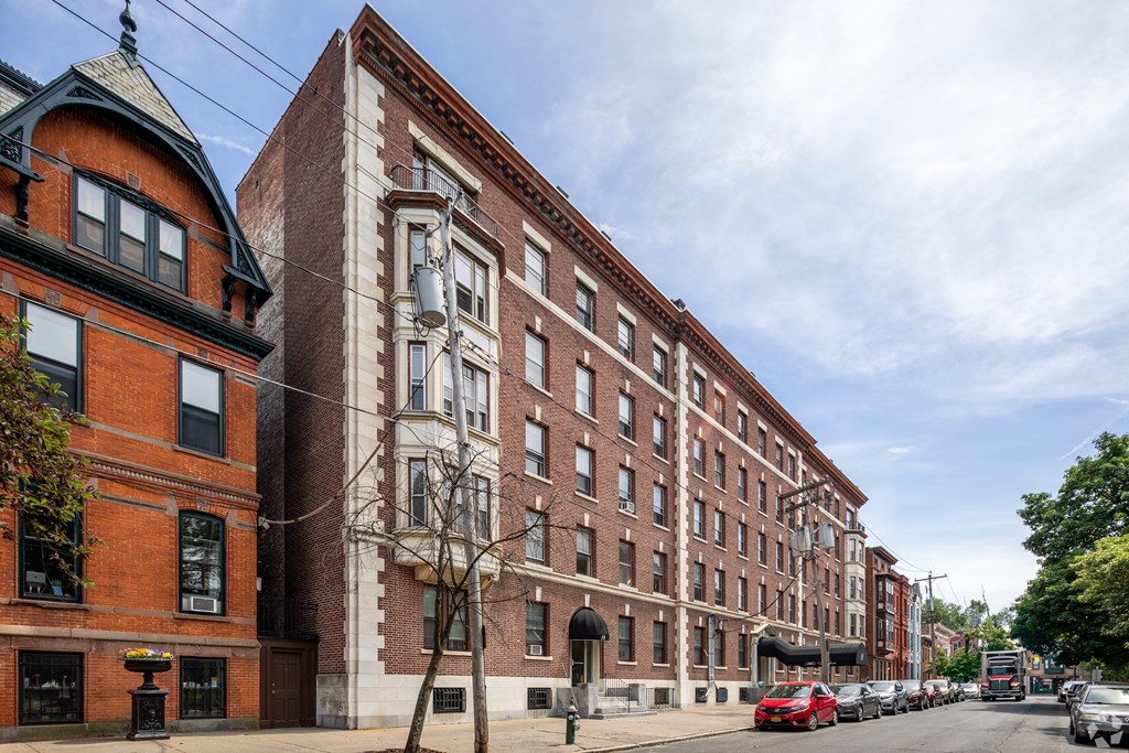 A row of red brick buildings line a tree-lined street. at Willett Apartments, Albany, NY, 12210
