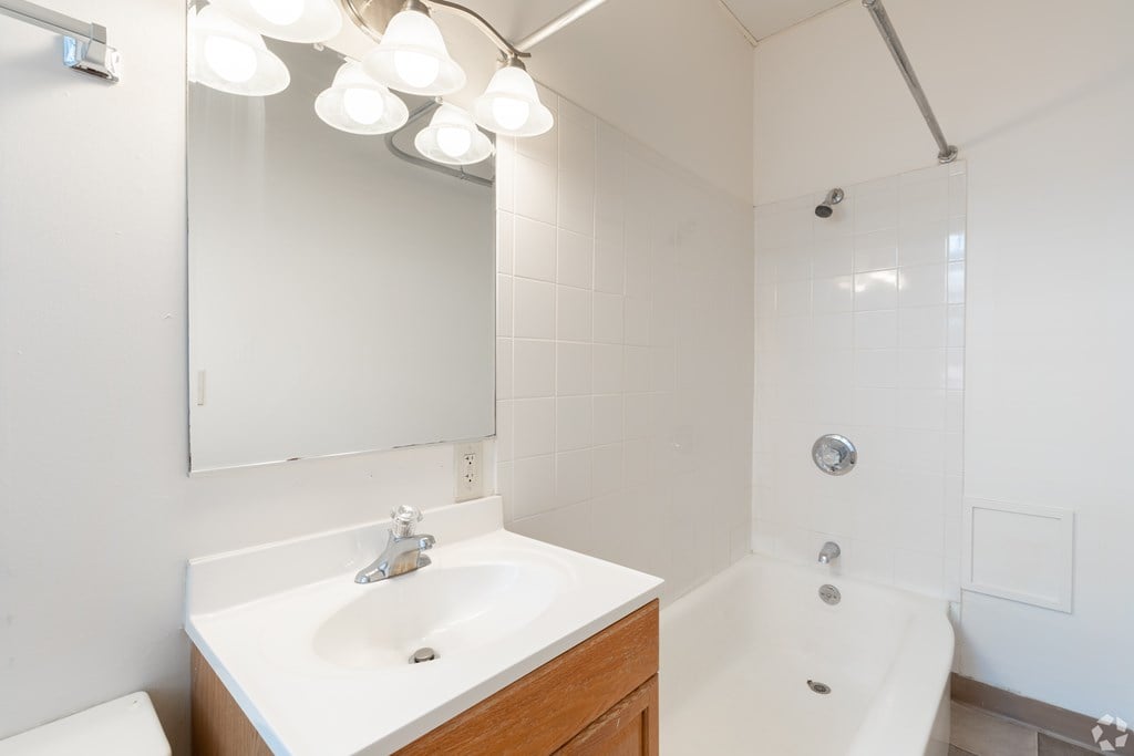 A white bathroom with a sink, mirror, and tub. at Willett Apartments, Albany, NY, 12210