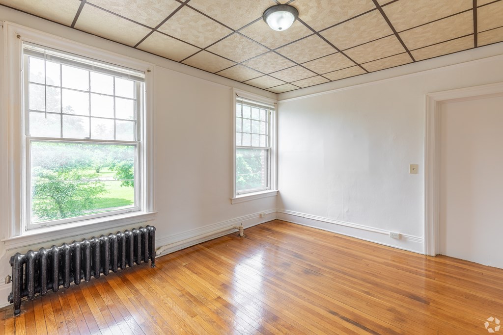 A room with a wooden floor and a window with a view of greenery outside. at Willett Apartments, Albany, NY, 12210